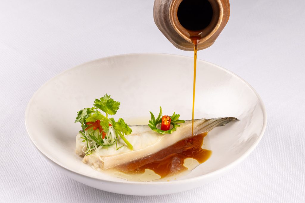 Visgerecht in een wit diep bord terwijl saus wordt ingeschonken — Restaurant O&O