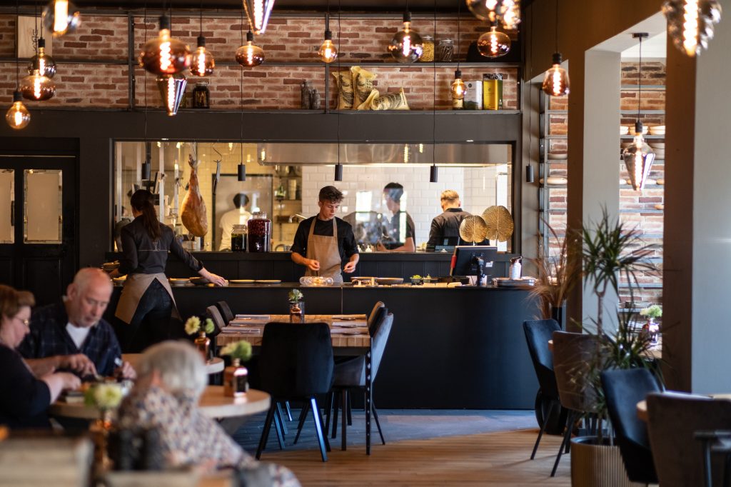 Restaurantinterieur met gasten, open keuken en houten tafels — Restaurant Promessa