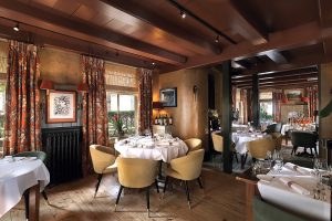 Restaurantzaal met gedekte ronde tafels, zichtbare houten plafondbalken en bloemen — Tante Koosje