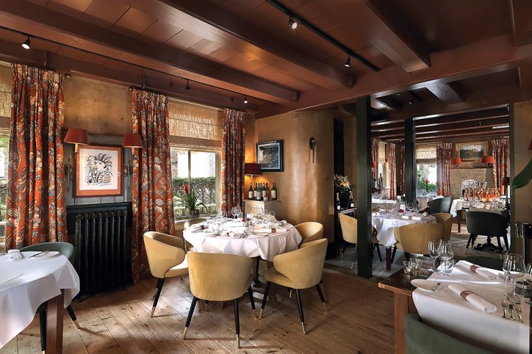 Restaurantzaal met gedekte ronde tafels, zichtbare houten plafondbalken en bloemen — Tante Koosje
