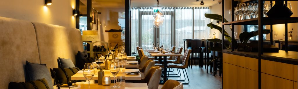 Gedekte tafels en zitbanken in het restaurant; breed panoramisch kader — Bij Erik