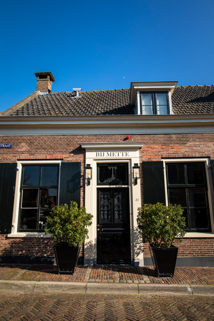 Bakstenen restaurantgevel met donkere luiken en entree; staand beeld — Restaurant Bij Mette