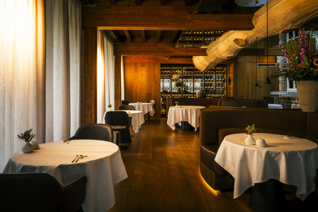 Warm verlichte eetzaal met ronde gedekte tafels en houten balken — Create by Guido Braeken