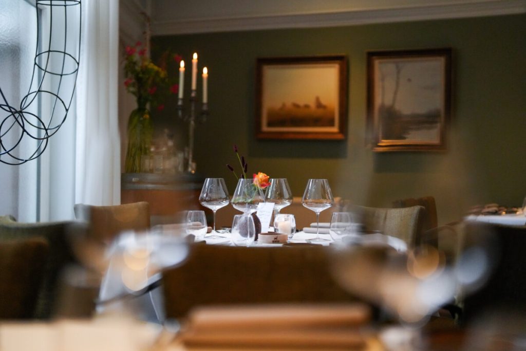 Gedekte tafels met wijnglazen, schilderijen en kaarslicht in het interieur van Olde Marckt — Olde Marckt