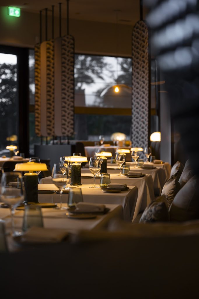 Gedekte restauranttafels met warme lampjes in een donker interieur; verticale opname — Nami