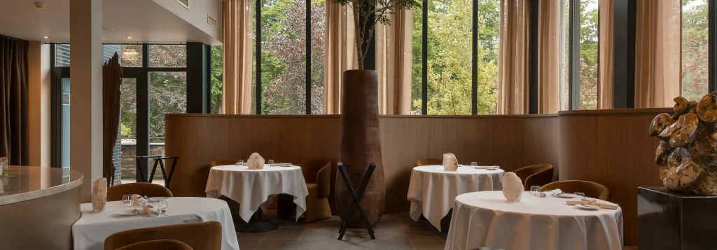 Gedekte ronde tafels en grote ramen met uitzicht op bos — Wild Atelier