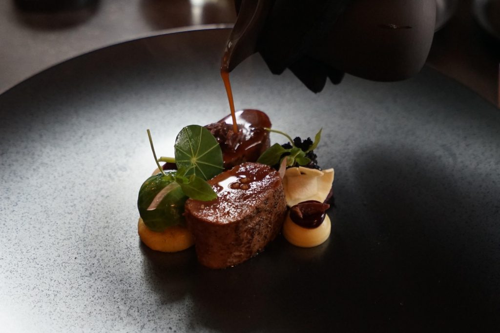Gerecht op een donker bord wordt aan tafel met saus afgewerkt — Sabero