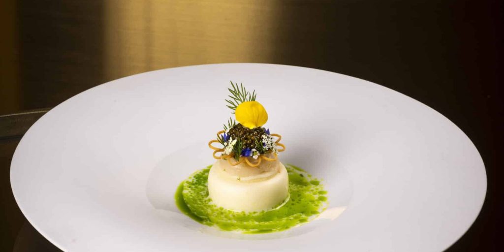 Fijn opgemaakt gerecht op een wit bord, geel bloemetje en groene saus — Restaurant Voltaire