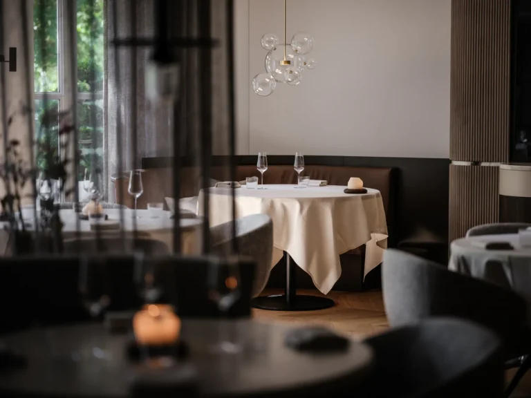 Sfeervol verlichte fine-diningzaal met ronde gedekte tafels en grote ramen — Alma Fine Dining
