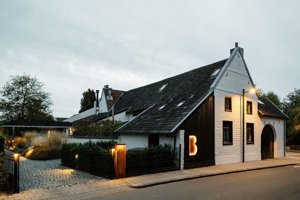 Verlichte restaurantgevel met wit pleisterwerk in de schemering — De Leuf