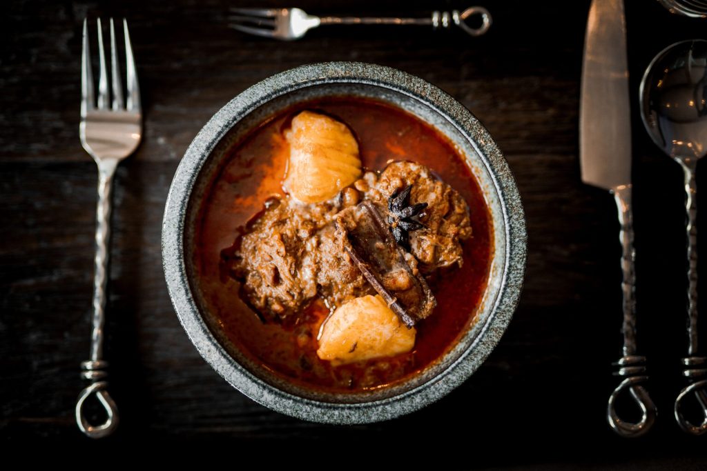 Thaise curry met vlees en aardappel in een donkere kom, gefotografeerd van boven — Reua Thai