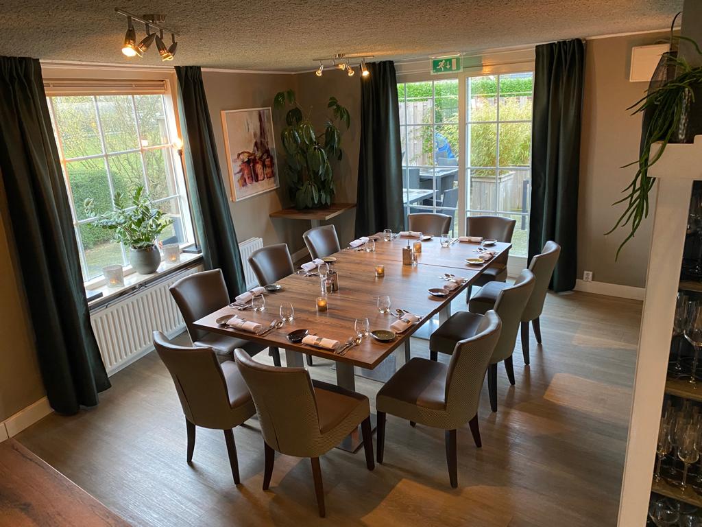 Licht restaurantinterieur met een lange gedekte tafel en zicht op het terras — De Schans by Mike & Wes