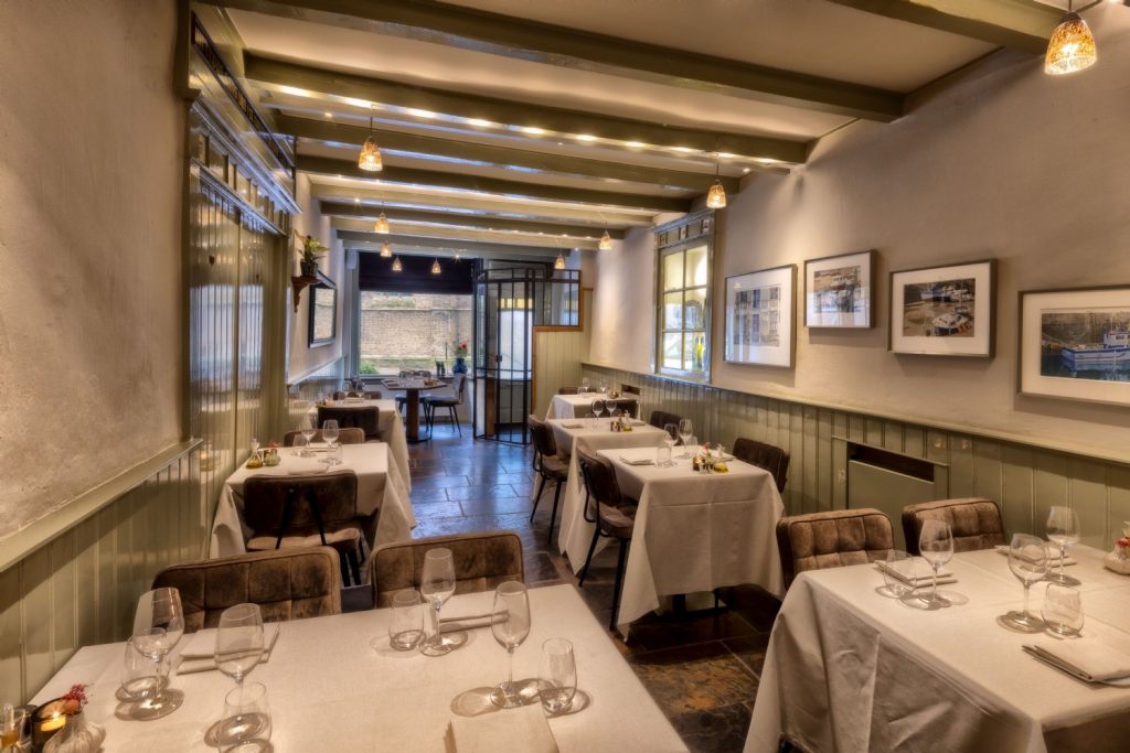 Sfeervolle langgerekte eetzaal met balkenplafond en gedekte tafels.