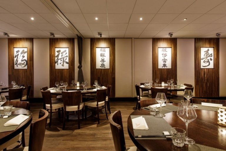 Eetzaal met ronde tafels, donkere stoelen en Chinese kalligrafie.