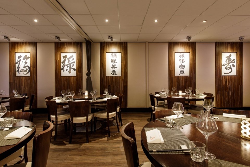 Eetzaal met ronde tafels, donkere stoelen en Chinese kalligrafie.