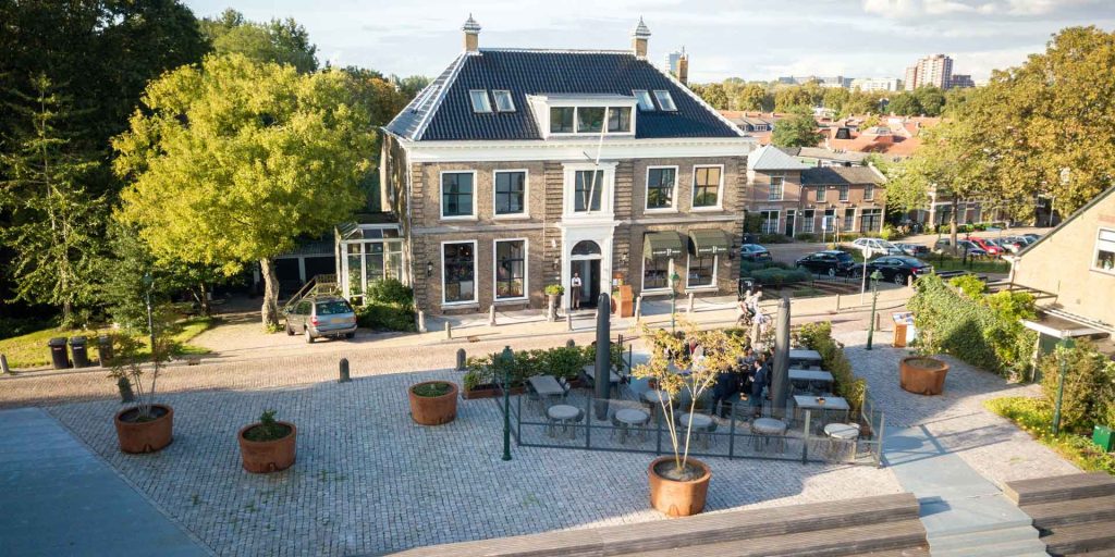 Monumentaal restaurantgebouw en terras, van boven gefotografeerd.