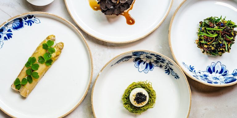 Vier verfijnde gerechten op wit-blauwe borden.