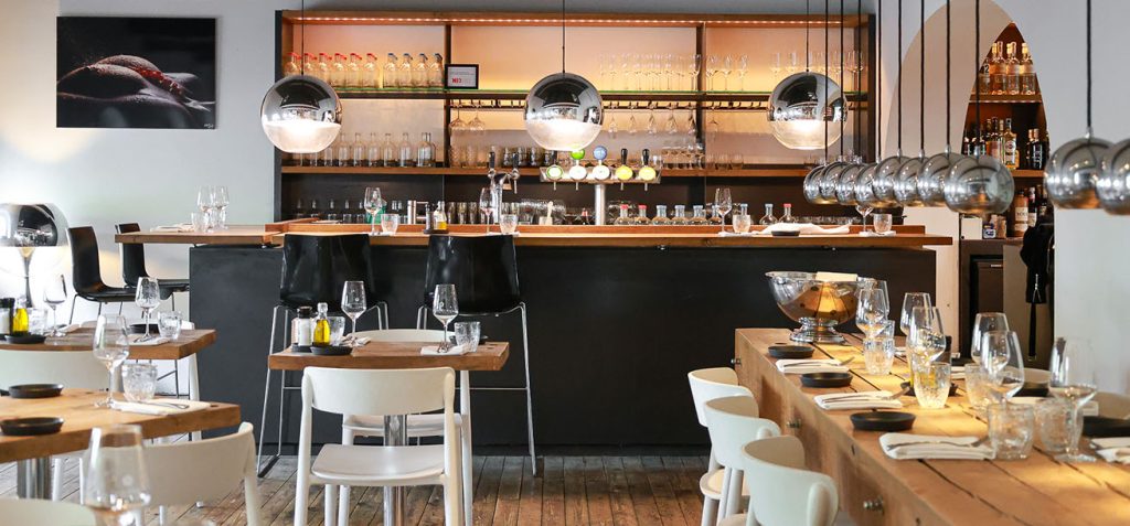 Overzicht van restaurantzaal en bar met gedekte houten tafels.