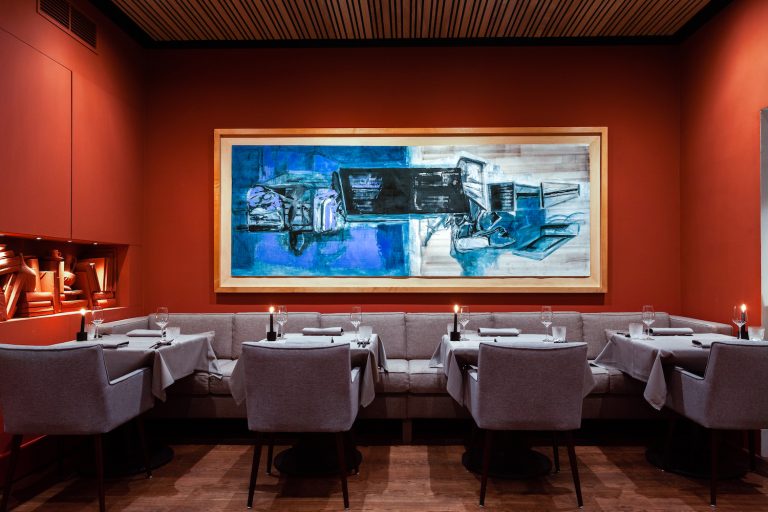 Restaurantinterieur met donkerrode muren, gedekte tafels en kunstwerk.