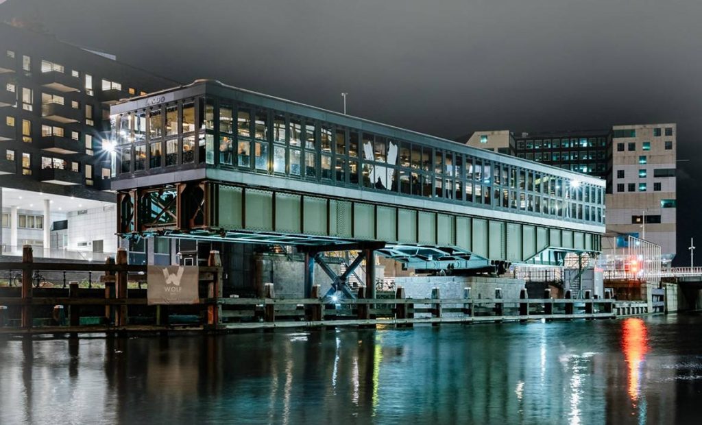 Wolf Atelier in een glazen gebouw aan het water bij avondlicht.
