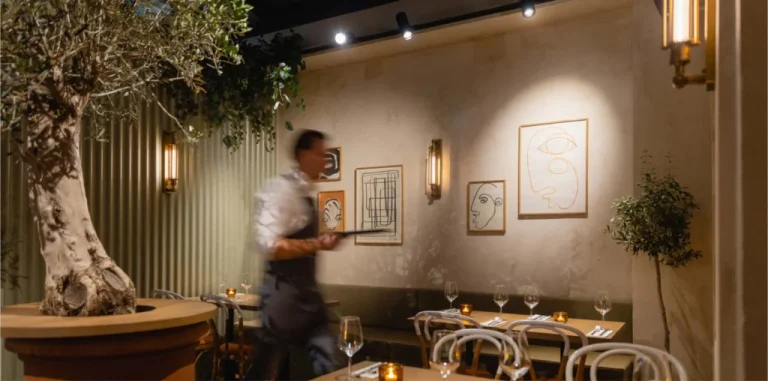 Restaurantinterieur met houten stoelen, gedekte tafels en boomdecoratie.