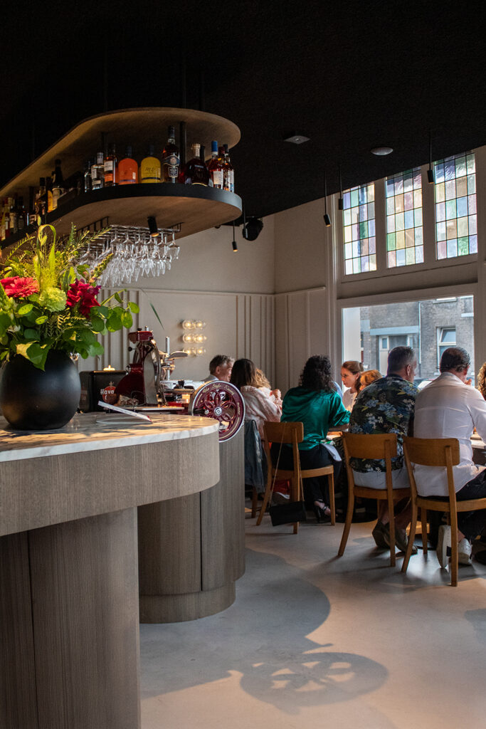 Restaurantinterieur met bar en gasten aan houten tafels.