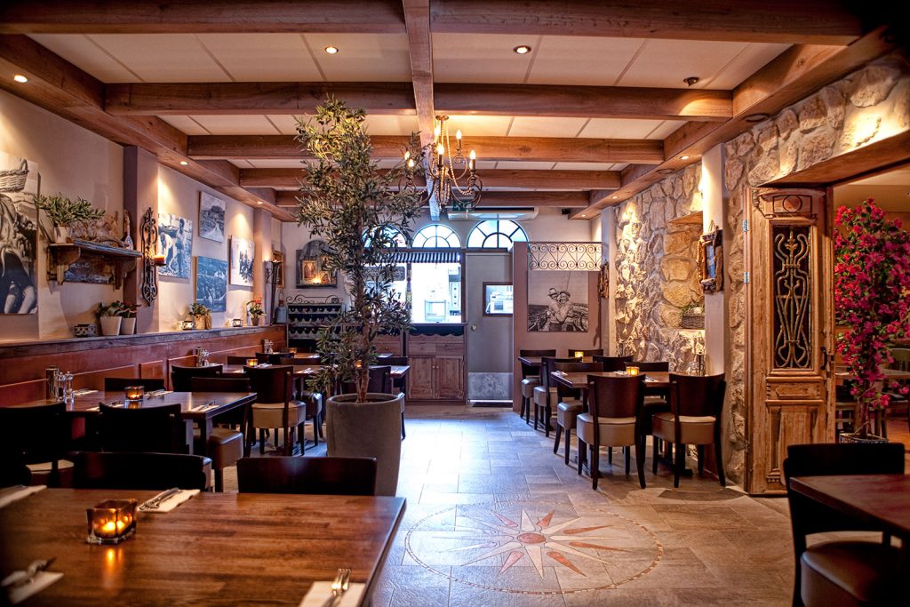 Restaurantzaal met houten balken, tafels en stoelen.