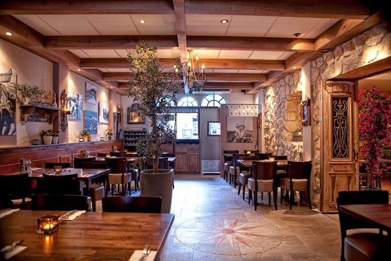 Restaurantzaal met houten balken, tafels en stoelen.