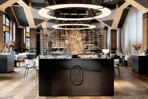 Restaurantinterieur met centraal meubel, wijnkast en ronde plafondlampen.