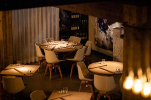 Warm verlichte eetzaal met ronde gedekte tafels.