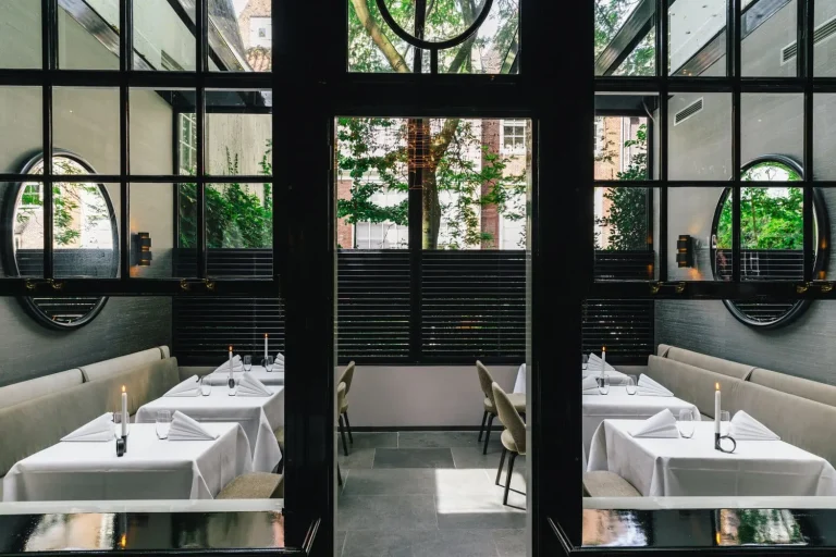 Intieme witte eetzaal achter glas met uitzicht op groen.