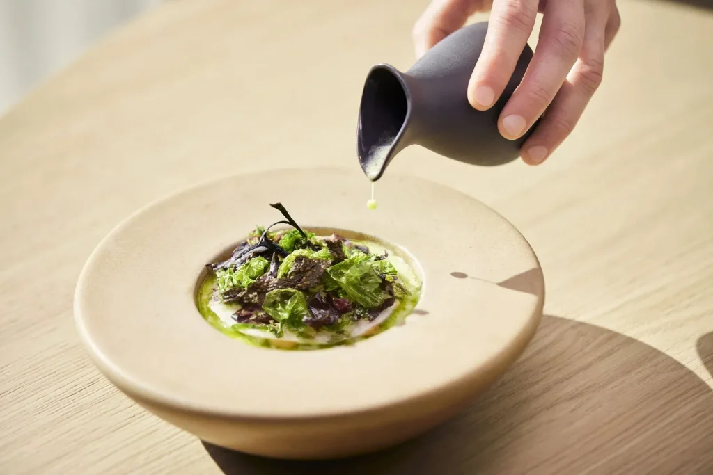 Groen gerecht in een ondiepe kom terwijl saus wordt ingeschonken.