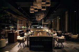 Restaurantinterieur met ruime zitgroepen, planten en geometrische plafondpanelen.