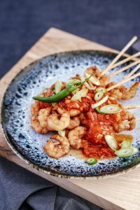 Gerecht met spiesjes en garnalen op blauwgrijs bord, op de Utrechtse menupagina.