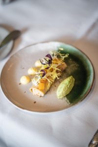 Fijn opgemaakt gerecht met groene saus en kleine bloemblaadjes in een keramieken kom.