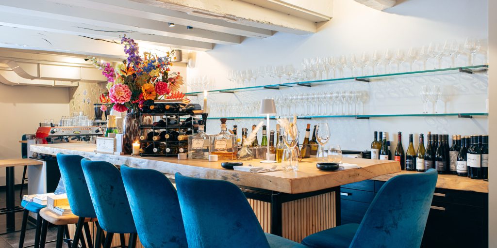 Bar met blauwe stoelen, bloemen en flessen.