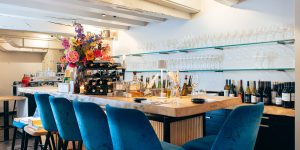 Bar met blauwe stoelen, bloemen en flessen.