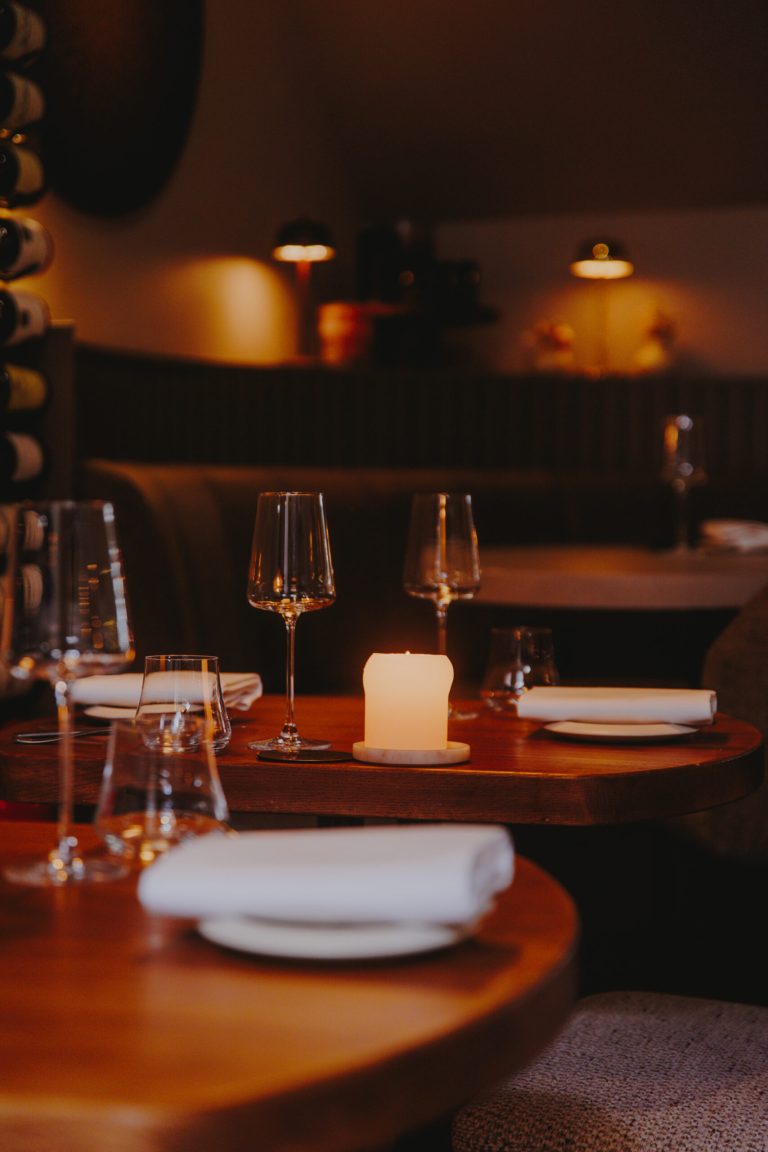 Warm verlichte restauranttafel met kaars en wijnglazen.