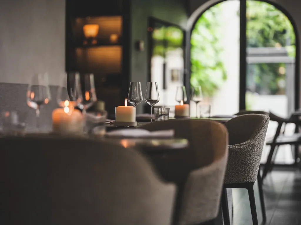 Gedekte tafels en stoelen in warm belichte bistro bij een raam.
