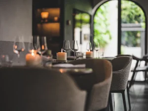 Gedekte tafels en stoelen in warm belichte bistro bij een raam.