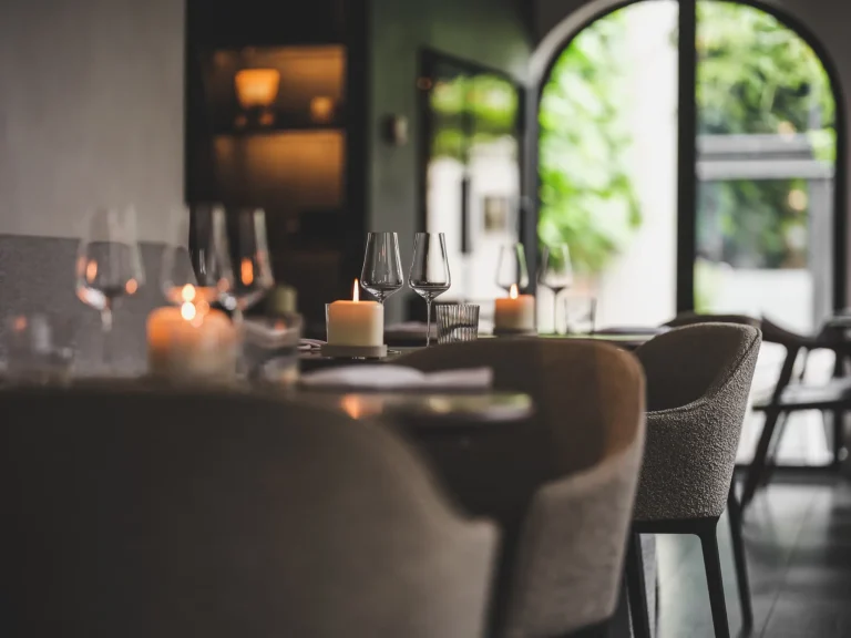 Gedekte tafels en stoelen in warm belichte bistro bij een raam.