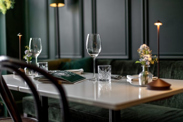 Gedekte bistrotafel met groen fluweel, donkere lambrisering, kaarsen en wijnglazen.