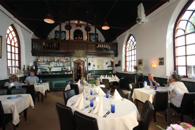 Restaurantzaal in een kerkgebouw met hoge rondboogramen.