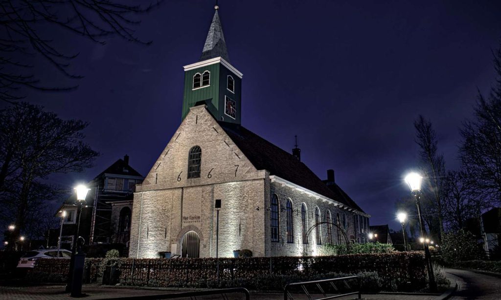 Verlicht kerkgebouw met torenspits in de avond.
