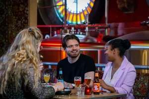 Gasten aan tafel binnen Jopenkerk, met glas-in-lood en brouwerijachtergrond.