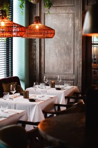 Restaurantinterieur met wit gedekte tafels en warme hanglampen.