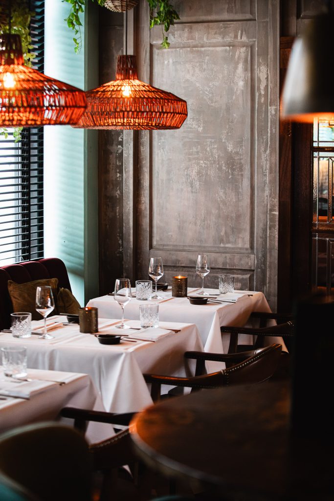 Restaurantinterieur met wit gedekte tafels en warme hanglampen.