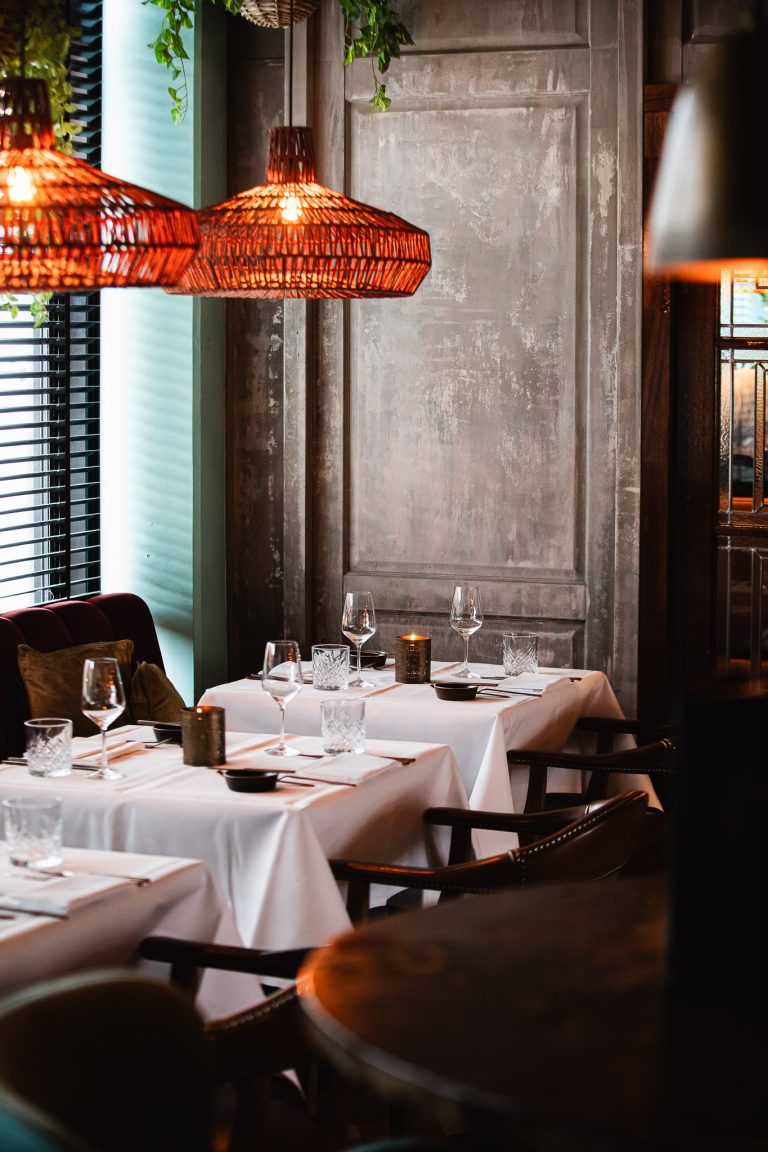 Restaurantinterieur met wit gedekte tafels en warme hanglampen.