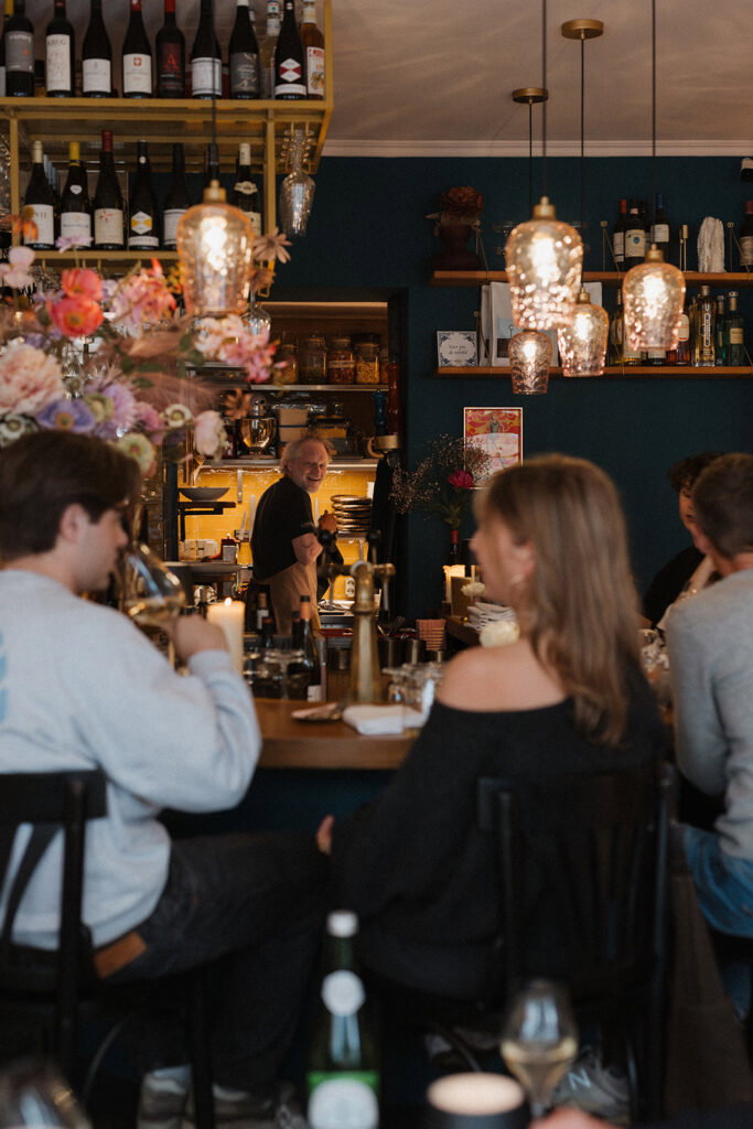 Restaurantinterieur met gasten aan de bar en hanglampen.