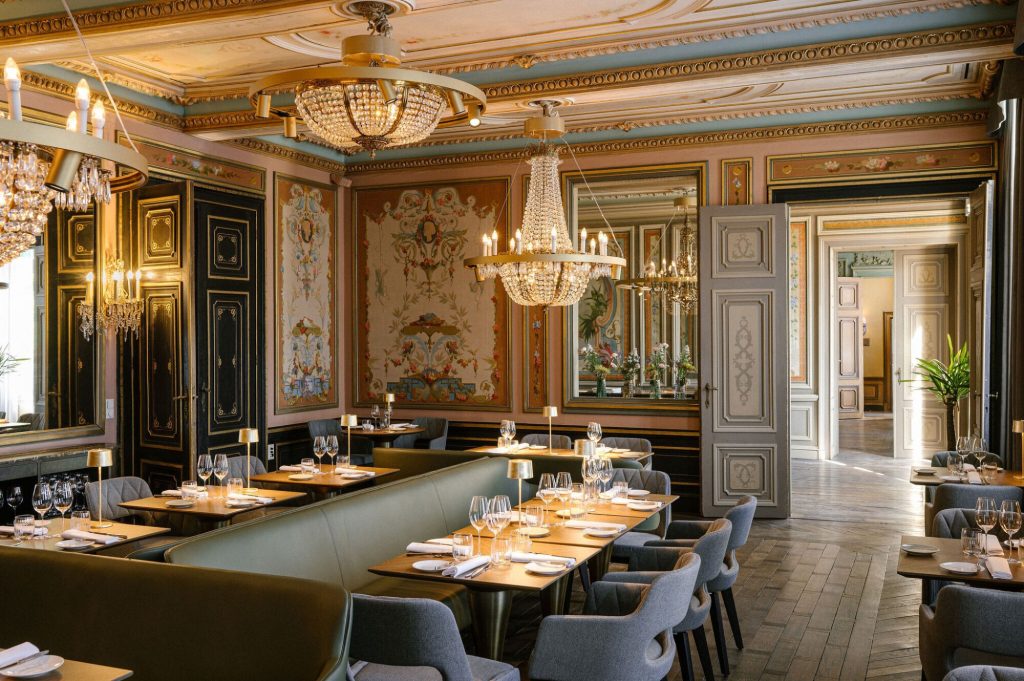 Klassieke restaurantzaal met muurschilderingen, kroonluchter en gedekte tafels.